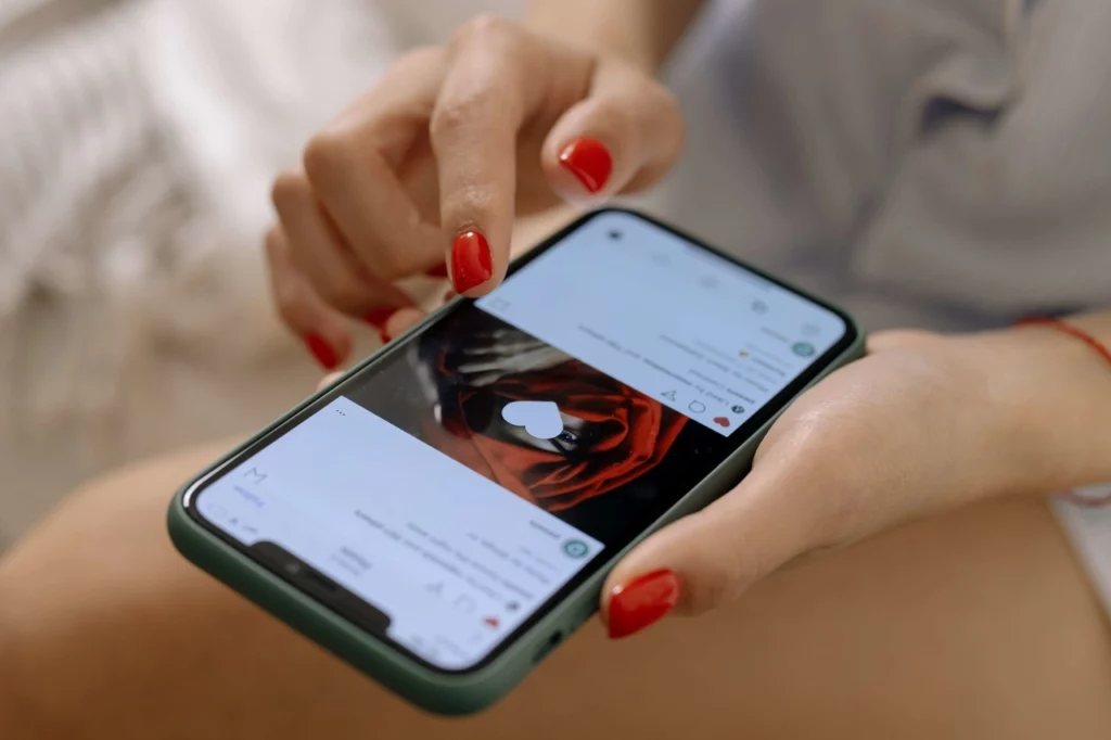 pessoa com unhas pintadas de vermelho segurando celular e curtindo uma foto no Instagram